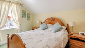 A bedroom with a wooden headboard, floral bedding, two bedside lamps, a bedside table with a lamp, and a window with curtains. - Edlington Hall Cottage (Edlington)