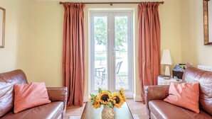 A living room with two brown leather sofas, a wooden coffee table with a vase of sunflowers, and a view of an outdoor patio through a glass door. - Edlington Hall Cottage (Edlington)