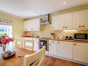 A kitchen with white cabinets, a wooden countertop, a stainless steel range hood, a microwave, and a sink.