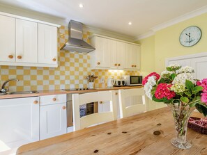 A kitchen with white cabinets, a microwave, and a sink. There is a vase with flowers on the table. - Edlington Hall Cottage (Edlington)