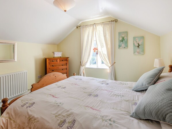 A bedroom with a bed, a dresser, a window with curtains, and a radiator.