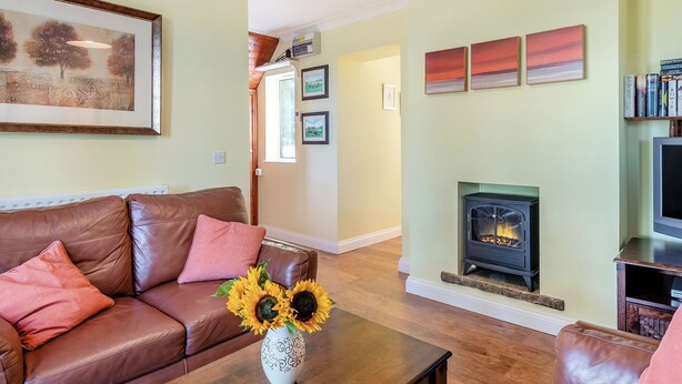 A living room with a brown leather sofa, a coffee table with a vase of sunflowers, a fireplace, and a bookshelf. - Edlington Hall Cottage (Edlington)