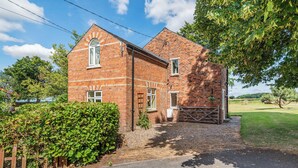 A brick house with a large window and a door, surrounded by a well-maintained lawn and a wooden fence. - Edlington Hall Cottage (Edlington)