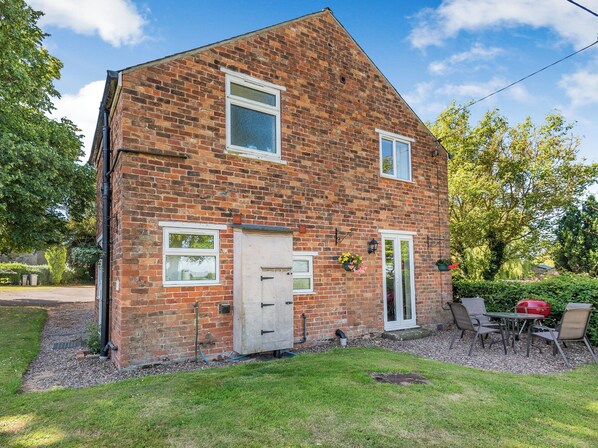 A brick house with a front door, two windows, and a small garden area with a table and chairs.