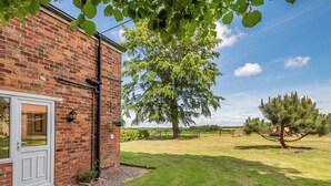 A brick building with a white door, a small garden with a tree, and a clear sky. - Edlington Hall Cottage (Edlington)