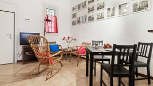 Una sala de estar con televisor, sillas de mimbre, una mesa de comedor con sillas negras y una pared decorada con fotografías en blanco y negro.