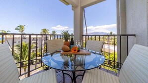 A glass-top table with chairs on a balcony, a bottle, a pineapple, and a flower arrangement. - SUMMER SALE! 2BD Condo Across Beach Ocean View AC Pool - AKH D402 (Kihei)