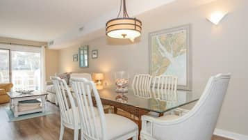 A dining area with a glass table surrounded by white chairs, a hanging light fixture, and a large framed map on the wall.