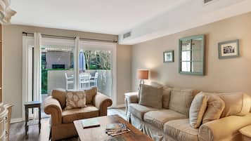 A living room with two beige sofas, a wooden coffee table, and a large sliding glass door leading to an outdoor patio.
