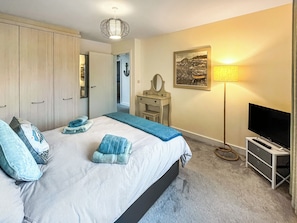 Ein Schlafzimmer mit Bett, Schreibtisch, Fernseher, Lampe und einem Bild an der Wand.