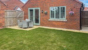 Une maison en briques avec une porte verte, une fenêtre et un patio aménagé avec du mobilier d’extérieur.