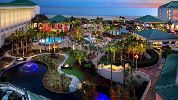 A resort with multiple swimming pools, palm trees, and a view of the ocean.