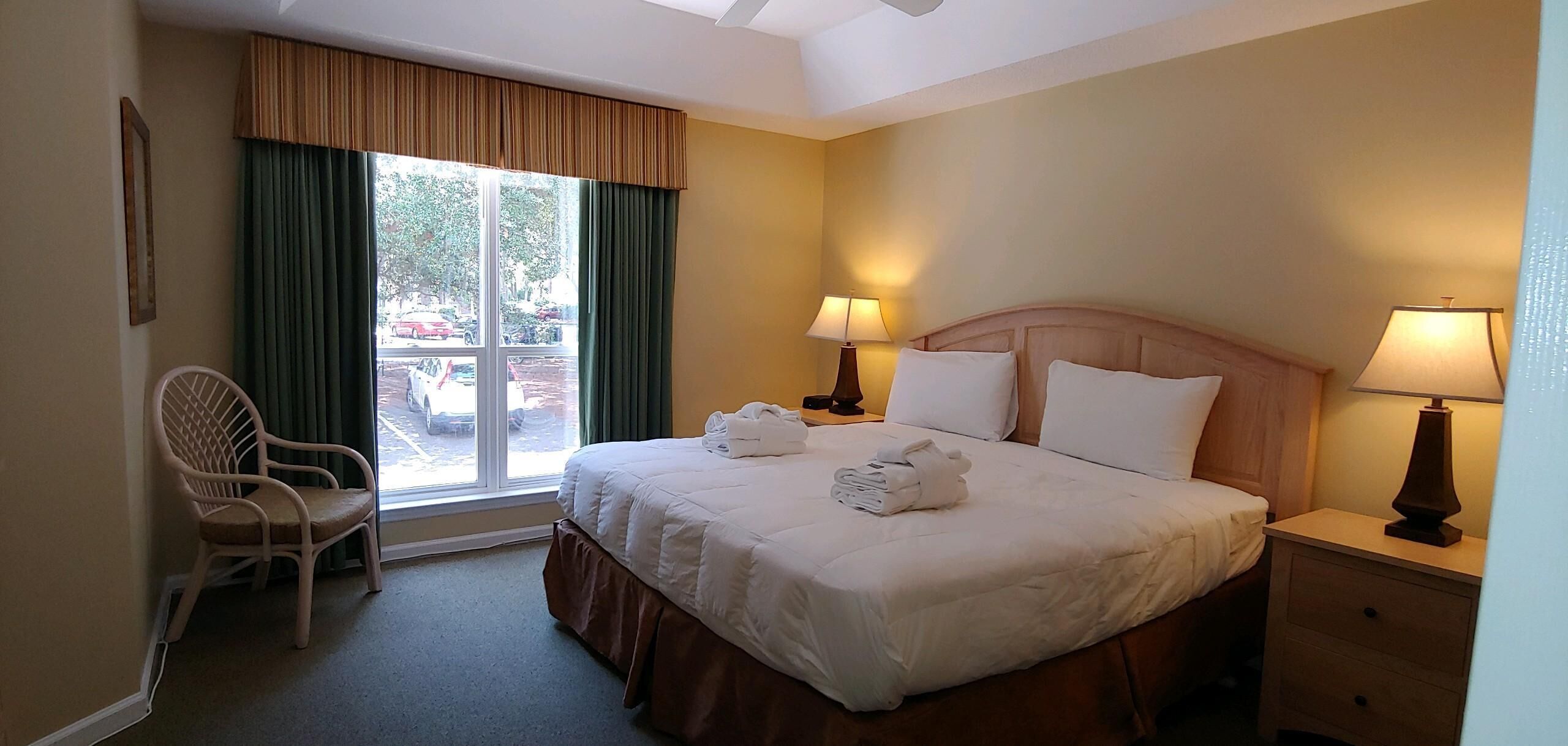 Una camera d'albergo con un letto grande, due abat-jour, una poltrona e una finestra con tende.