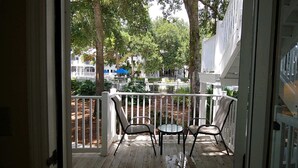 A wooden deck with two chairs and a table, surrounded by white railings and trees.