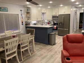 Cocina moderna con armarios blancos, una isla central, electrodomésticos de acero inoxidable y una zona de comedor con sillas de madera.