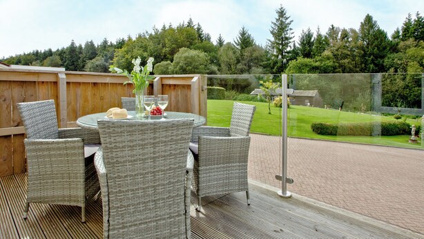 Une terrasse extérieure aménagée avec des meubles en osier, une table en verre et une vue sur un jardin et des arbres.