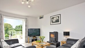 Un salon moderne avec des canapés en cuir, un téléviseur, une cheminée et une vue sur la verdure à l’extérieur.