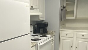 Cozinha com armários brancos, fogão, geladeira e cafeteira.