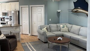A modern living room with a sectional sofa, a coffee table, a ceiling fan, and a mounted fish head on the wall. - Custom Home on LakeFront in Ocean Lakes (Myrtle Beach)