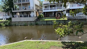 A waterfront property with a grassy area, a pond, and a multi-story building with balconies. - Custom Home on LakeFront in Ocean Lakes (Myrtle Beach)