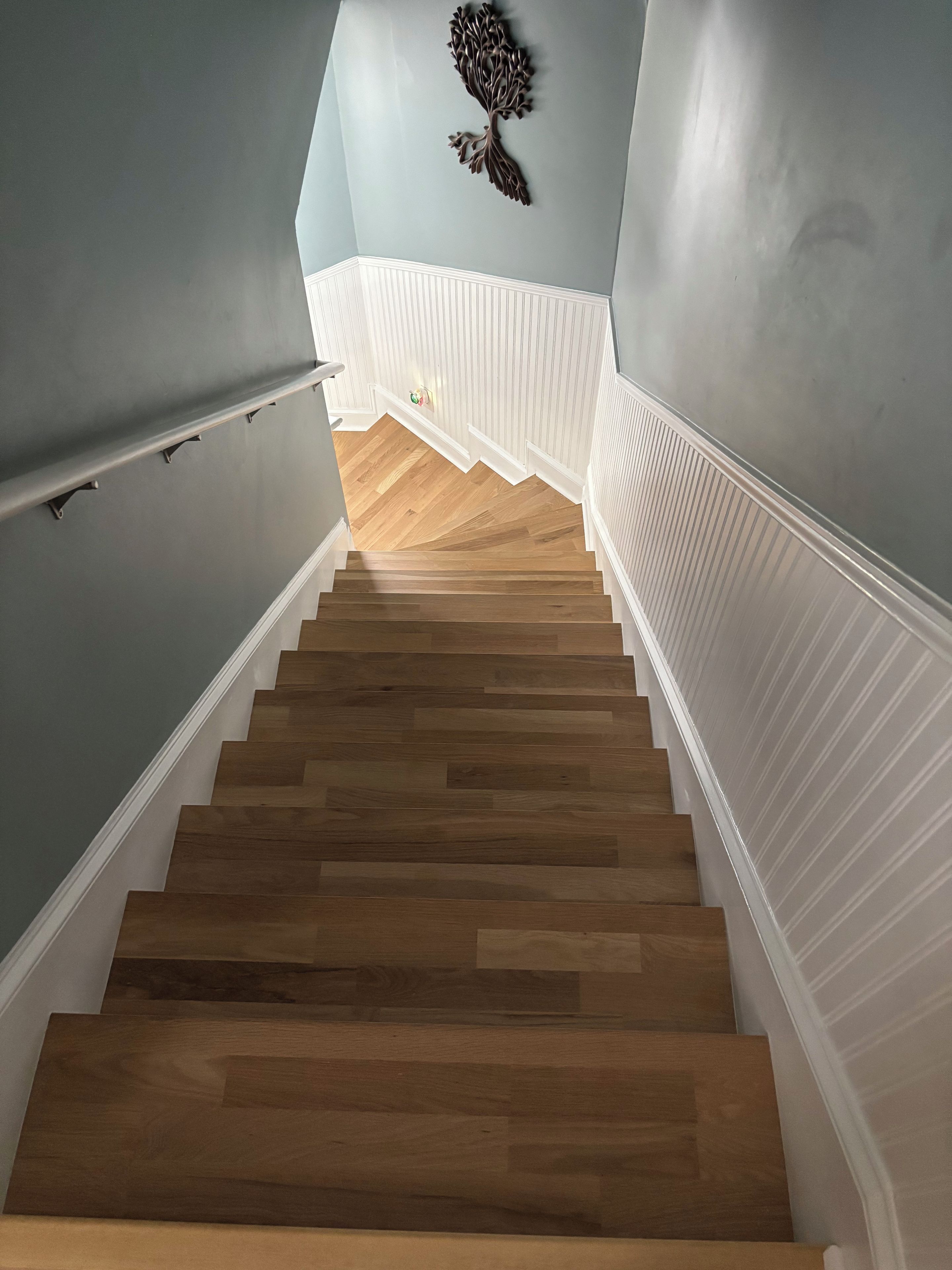 Una escala amb graons de fusta i fustes decoratives, que condueix a una habitació amb una paret de blau clar i un element decoratiu penjat.