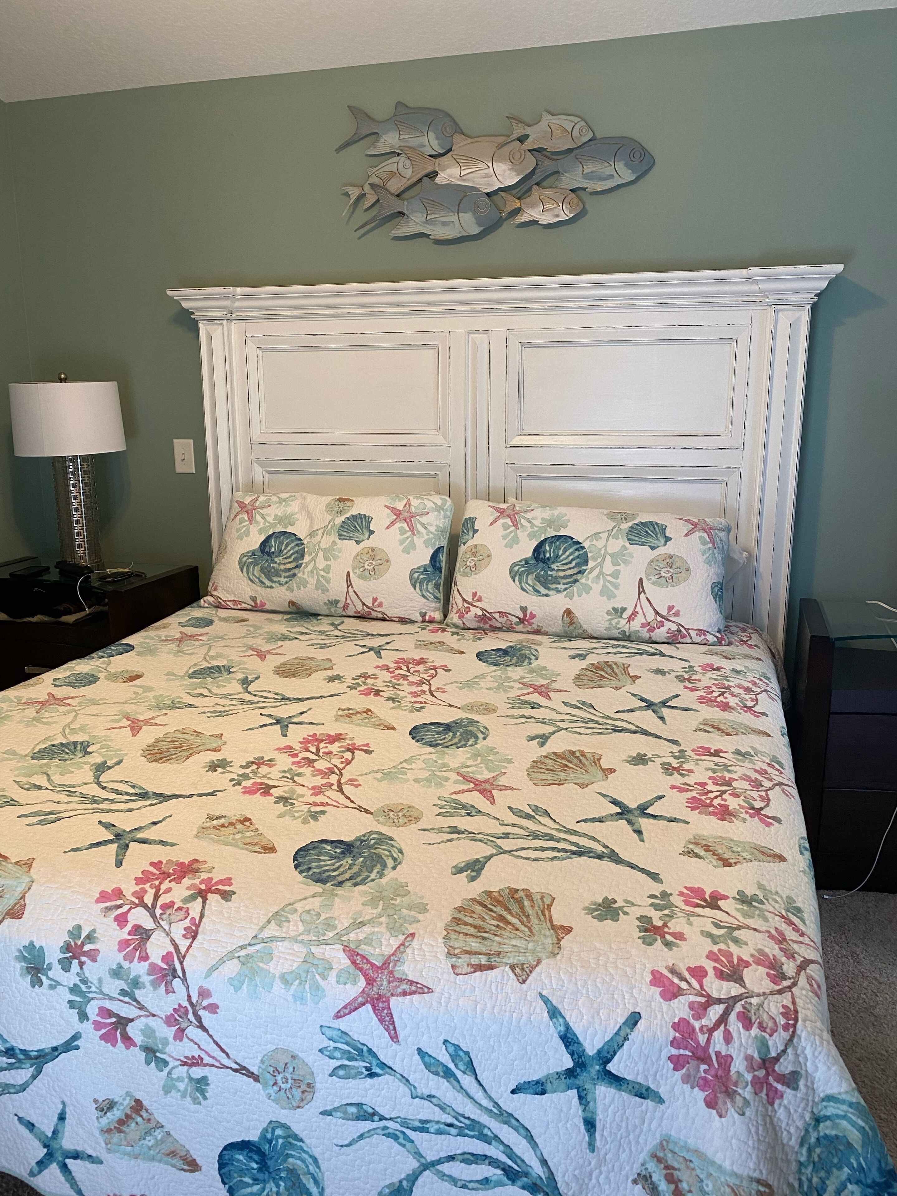 A bedroom with a floral bedspread, a white headboard, and a wall decoration of fish.