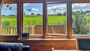 A room with large windows overlooking a green field, a wooden deck, and a view of the sky with birds. - 2 bedroom accommodation in Black Isle (Black Isle)
