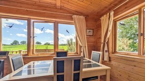 A wooden cabin with a glass-top dining table, chairs, and large windows offering a view of the sky and greenery. - 2 bedroom accommodation in Black Isle (Black Isle)
