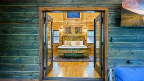 Interior de una cabaña de madera con una cama, paredes de madera y un cuadro en la pared.