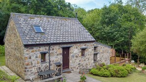 A stone cottage with a sloped roof, a wooden door, and a small porch with a table and chairs.