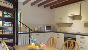 A kitchen with white cabinets, a microwave, and a stove. There is a wooden dining table with chairs and a fruit bowl on it.