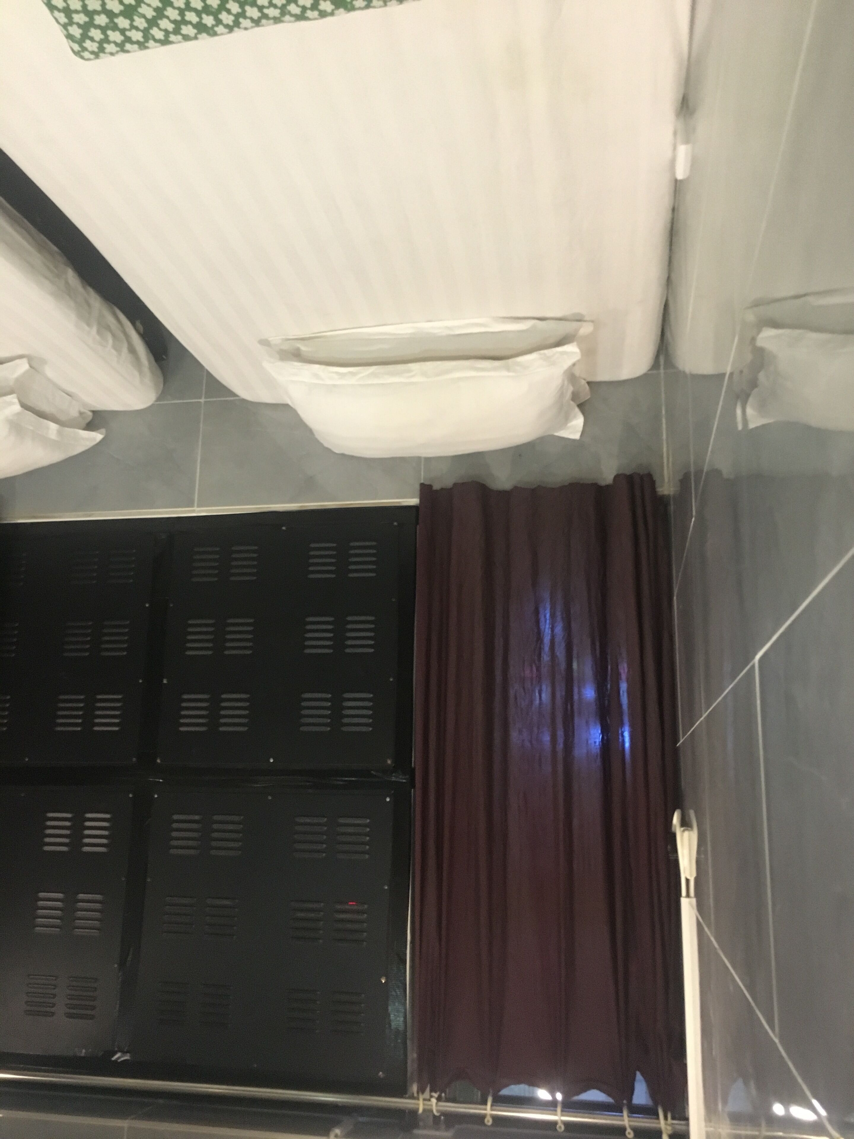 Una habitación con piso de baldosas, un mueble de almacenaje negro, un techo blanco con diseño verde y una cortina oscura.