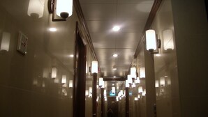 Un couloir d’hôtel avec de nombreuses portes, un éclairage encastré et un miroir sur le mur de droite.