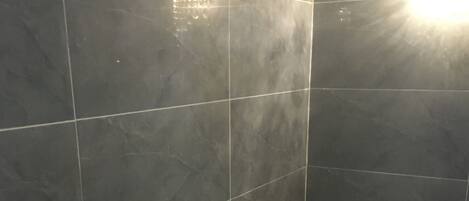 Un baño con baldosas gris oscuro, una toalla blanca y una alfombra de baño azul.