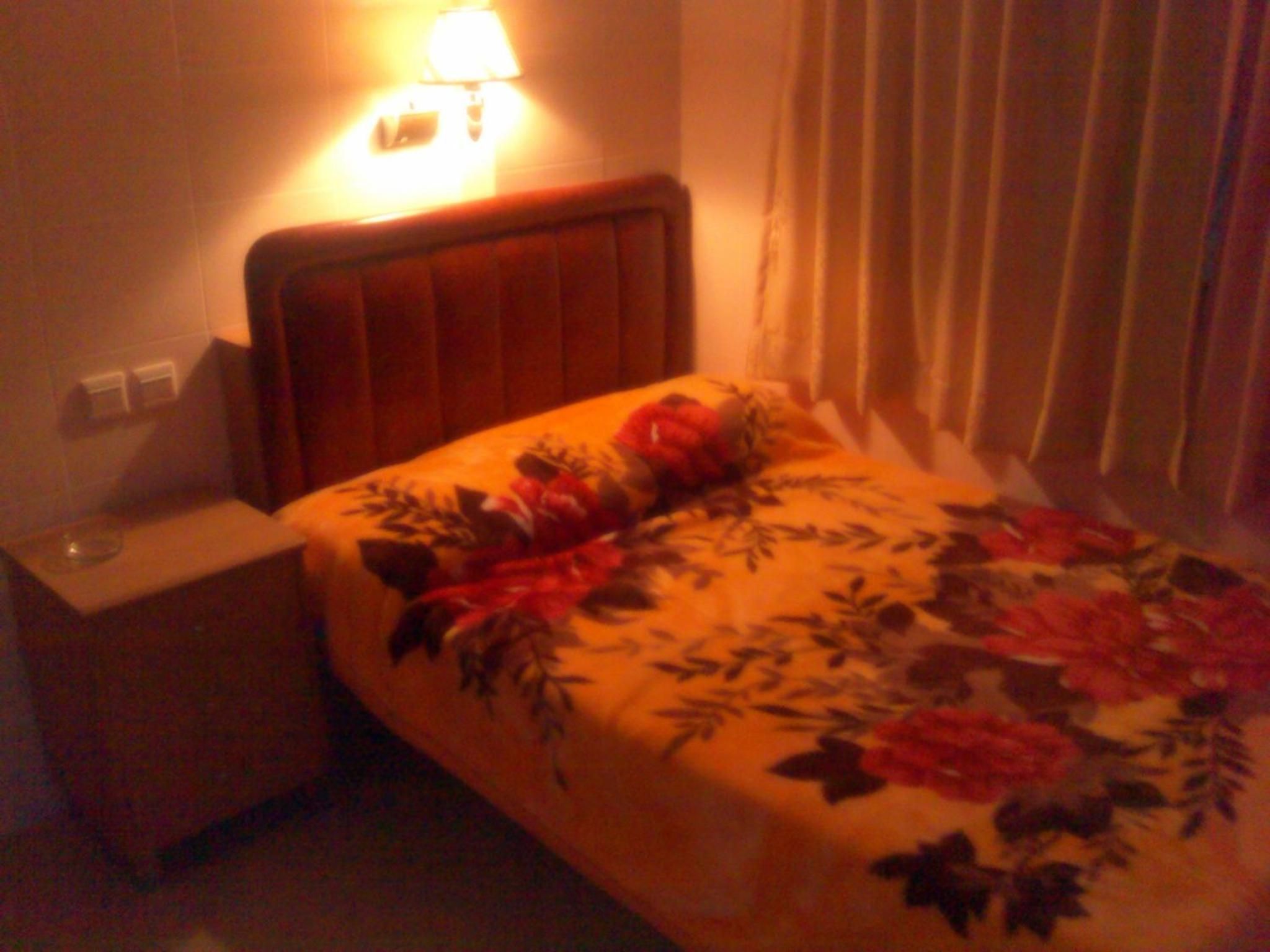 A hotel room with a bed, nightstand, lamp, and curtains.
