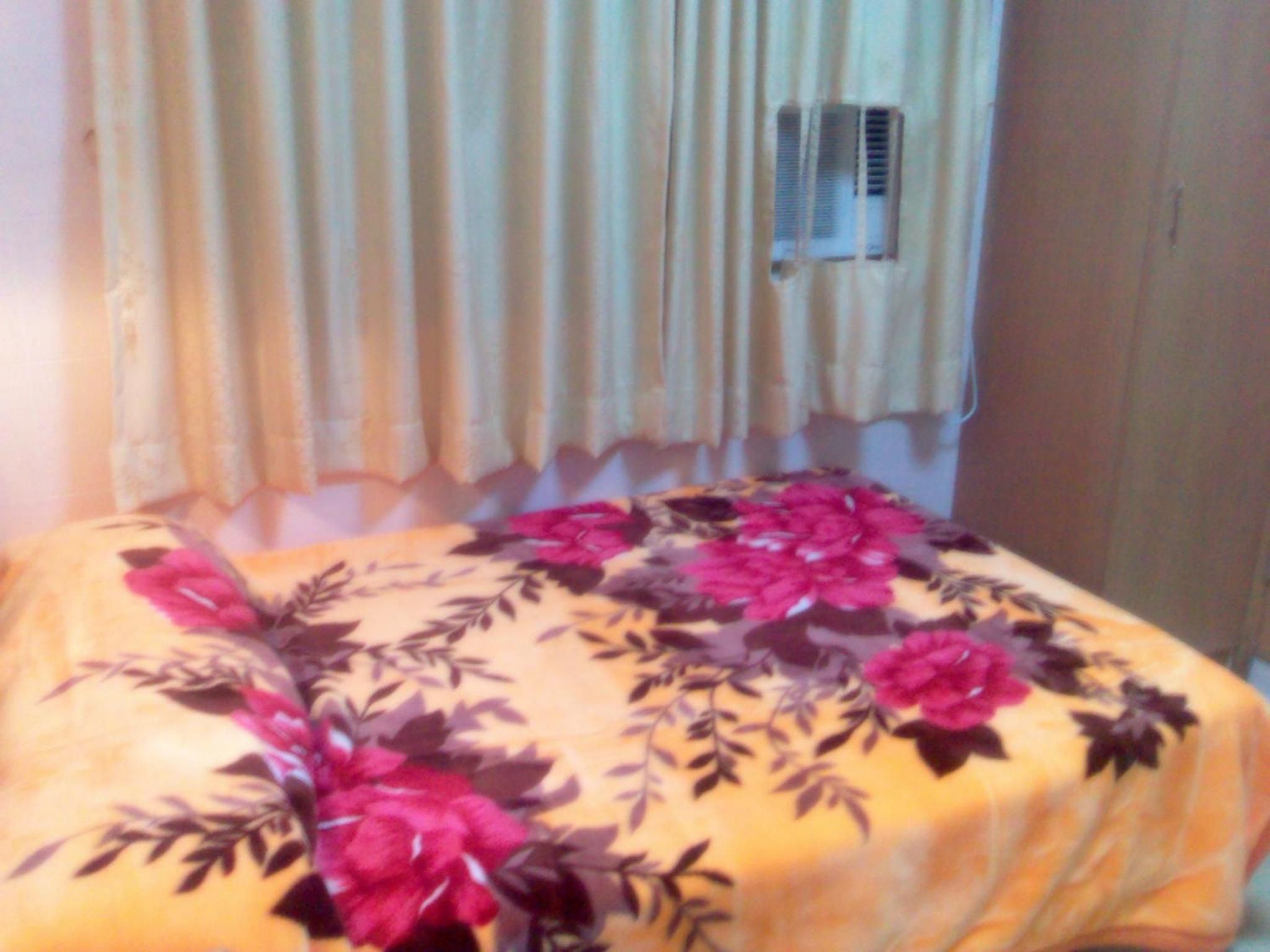 A bed with a floral bedspread, a window with curtains, and an air conditioning unit.