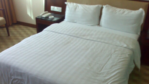 Un lit bien fait, avec du linge de lit blanc, dans une chambre d’hôtel.