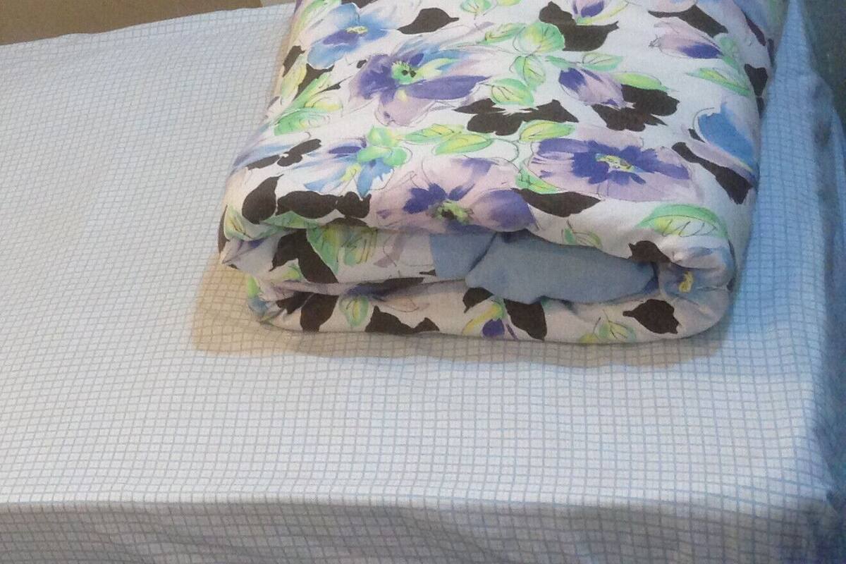 Una cama con sábana blanca y manta estampada.