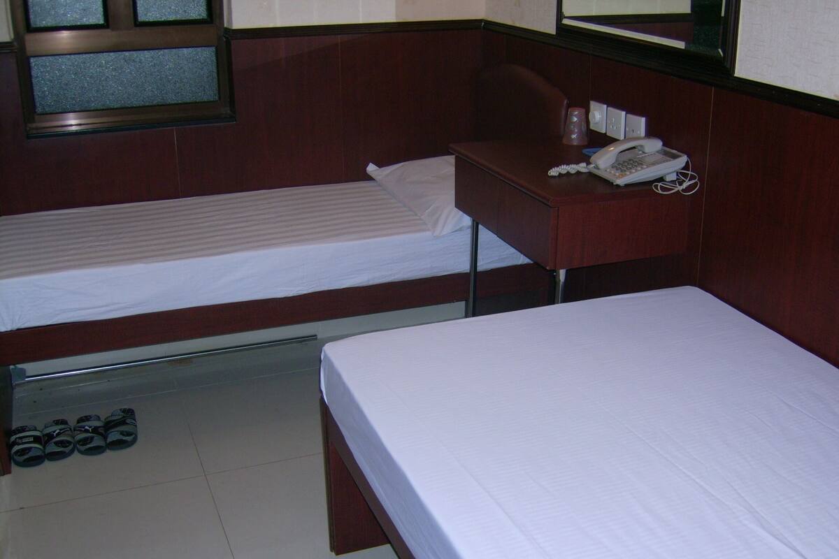 Una habitación de hotel con dos camas individuales, un escritorio con teléfono y un par de zapatos en el suelo.