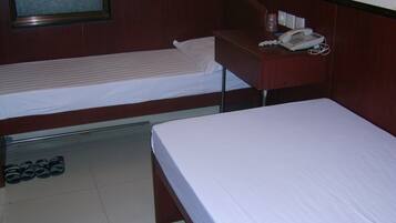 Ein Hotelzimmer mit zwei Einzelbetten, einem Schreibtisch mit Telefon und einem Paar Schuhe auf dem Boden.