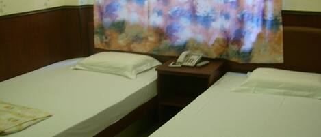 A hotel room with two single beds, a nightstand with a telephone, and a floral curtain.