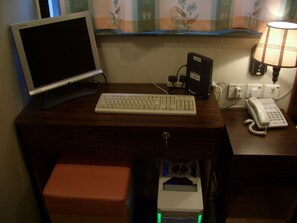A wooden desk with a computer monitor, keyboard, telephone, and a small device with a green light. - Hong Kong Coliving Space (Kowloon)
