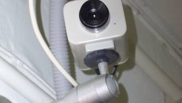 A bathroom with a camera mounted on the wall, a hand dryer, and a white pipe.