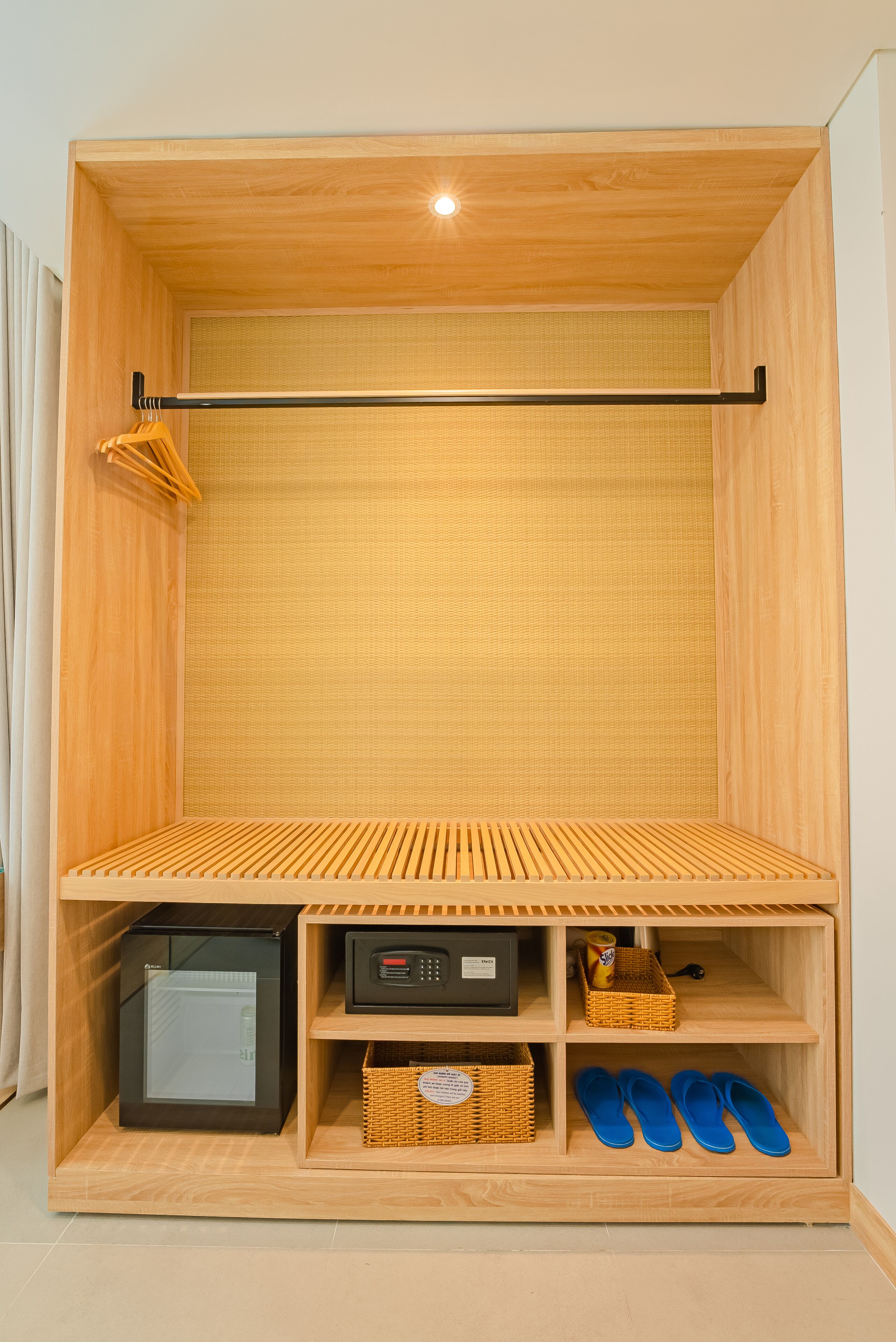 Un meuble de rangement compact avec un revêtement en bois, comprenant un petit réfrigérateur, un panier et une paire de chaussons.