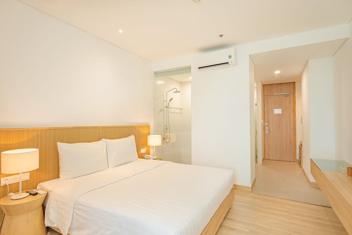 Een hotelkamer met een bed, nachtkastje, lamp en een douchehoek.