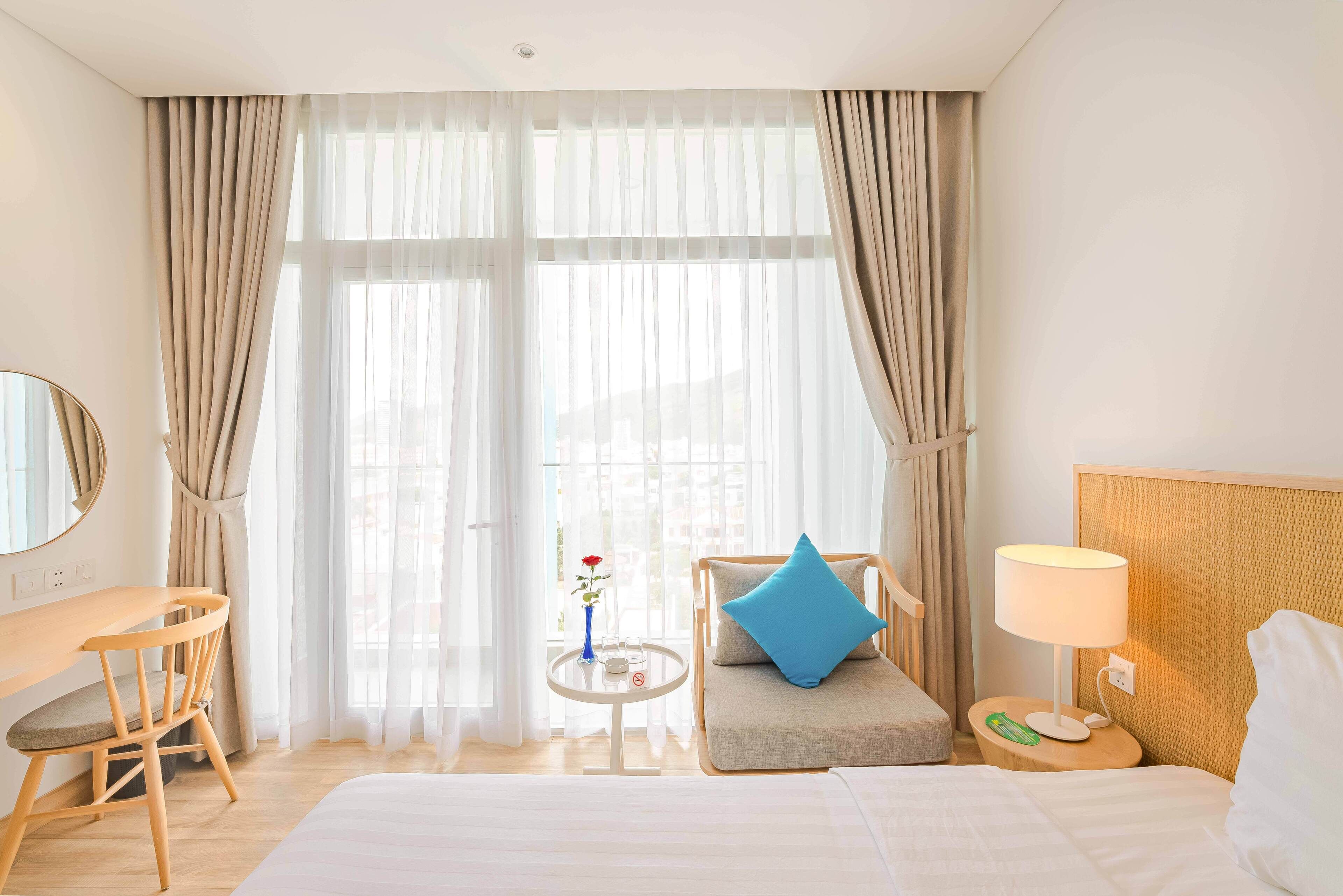 Habitación de hotel con cama, escritorio, silla, una mesita con un florero y una lámpara.