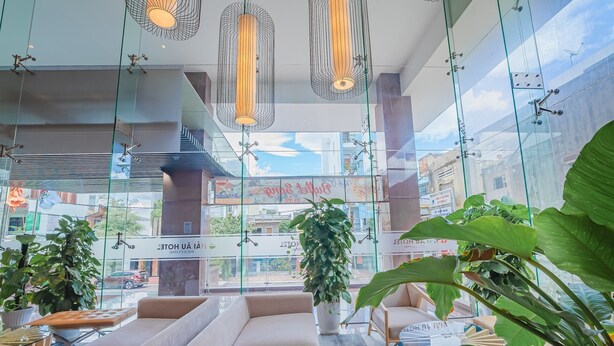 A modern hotel lobby with glass walls, seating areas, and hanging pendant lights.
