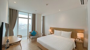 A hotel room with a large bed, a desk with a chair, a small table, and a TV.