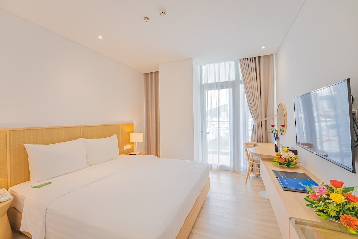 Een hotelkamer met een groot bed, een bureau met stoel, een flatscreen televisie en een raam met gordijnen.