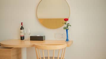 Escritorio de madera con un espejo, una botella de vino, una copa, una caja de pañuelos y un florero con una rosa.